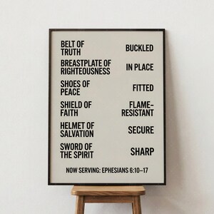 May include: A framed print with black text on a cream background. The text lists items such as "Belt of Truth" and "Breastplate of Righteousness" with corresponding action words. The bottom of the print reads "Now Serving: Ephesians 6:10-17".