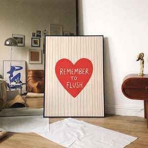 Funny bathroom decor print in frame on wall, Remember To Flush red heart typography poster displayed in modern living room interior with brown leather sofa and gallery wall, showing versatile home decor styling