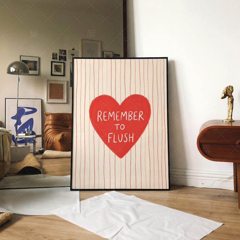 Funny bathroom decor print in frame on wall, Remember To Flush red heart typography poster displayed in modern living room interior with brown leather sofa and gallery wall, showing versatile home decor styling