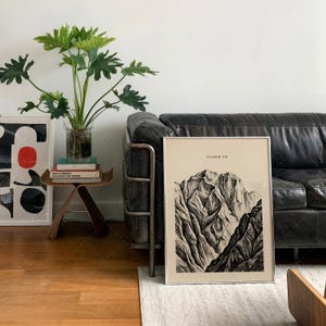 Climb On Mountain Print in frame on wall above leather sofa in contemporary living room, vintage mountain art poster with inspirational typography, nature landscape wall decor