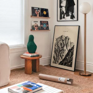 Climb On Mountain Print gift presentation in modern bedroom interior with mid-century furniture, vintage mountain landscape poster leaning against wall, minimalist adventure decor