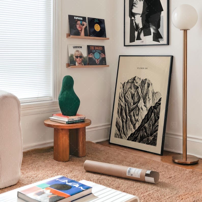 Climb On Mountain Print gift presentation in modern bedroom interior with mid-century furniture, vintage mountain landscape poster leaning against wall, minimalist adventure decor