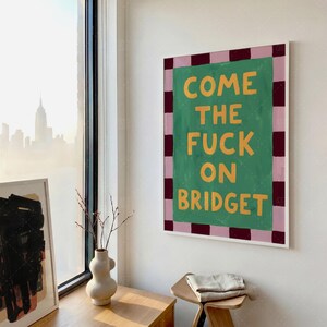 Come The Fuck On Bridget funny saying poster in frame on wall by window, retro wall art mockup in minimalist room with city view and wooden furniture