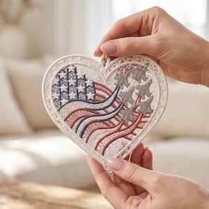 May include: A heart-shaped white lace ornament featuring an embroidered American flag design with blue stars and red and white stripes. The right side displays a formation of six grey fighter jets flying in a V-shape with trailing smoke lines.
