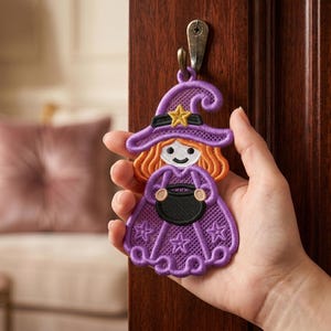 May include: A purple embroidered witch ornament featuring orange hair, a yellow star on the hat, and a black cauldron held in the center. The design includes a purple dress with star motifs and a scalloped hem, crafted with detailed stitching.
