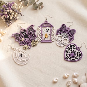 May include: Five embroidered earrings featuring Halloween motifs: a black bat with a purple rose, a white ghost inside a purple lantern, a white skull with a purple bow, a white ghost on a crescent moon, and a purple heart with a spider web.