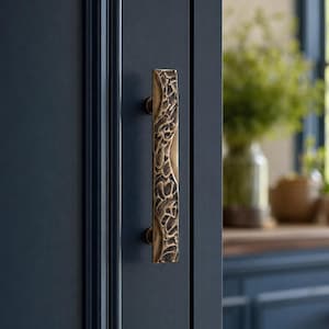 May include: A vertical cabinet pull handle with a textured, organic, bronze-toned finish mounted on a dark navy blue cabinet door. The handle features a rugged, uneven surface pattern that contrasts with the smooth, flat surface of the door.