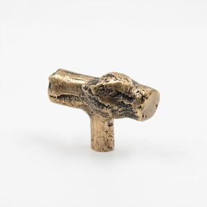 Peut inclure: Un bouton de meuble de couleur bronze avec un design texturé et organique. Le bouton a une forme en T, avec une base cylindrique et un dessus plus large et irrégulier, ressemblant à une petite branche. La finition a des accents sombres.