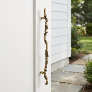 以下が含まれることがあります： 自然な枝のようなデザインのブロンズ色のドアプルハンドル。ハンドルは白いドアに取り付けられており、質感のある有機的な形状が特徴です。ドアハンドルは、家の装飾用の装飾要素です。