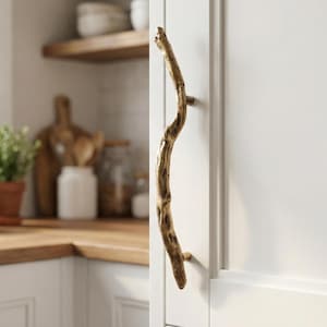 Può includere: Una maniglia per armadio a forma di ramo, color oro. La maniglia è montata su un'anta bianca. L'ambiente cucina comprende un piano di lavoro in legno, mensole e vari oggetti da cucina.