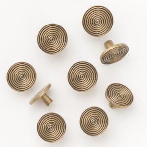 Op de afbeelding: Een verzameling messingkleurige kastknoppen met een spiraalvormig ontwerp. De knoppen zijn rond met een platte voorkant en een korte, cilindrische steel voor montage. Het spiraalpatroon is een opvallend kenmerk en creëert een textuur.