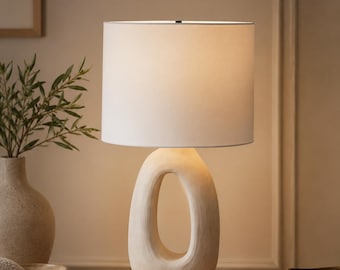 Skulptural bordslampa i harts, minimalistisk oval bas, skandinavisk linneskärm