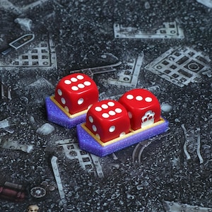 May include: Three red dice with white dots, resting on purple and gold platforms. The dice are arranged on a textured, dark gray surface, suggesting a tabletop game or hobby setting. The image is well-lit, highlighting the vibrant colors.