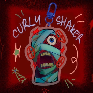 May include: A keychain with a cartoon mummy design. The mummy has a teal bandage, a wide open mouth, and a single blue eye. The keychain has the words "Curly Shaker" in white lettering and a blue clasp.