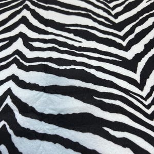 May include: A fabric featuring a high-contrast zebra print pattern with bold, irregular black stripes set against a stark white background. The textile displays a repeating organic design that covers the entire visible surface area of the material.