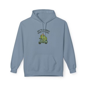 May include: A pale blue hoodie with a kangaroo pocket and a drawstring hood. The front displays a graphic of a frog on a scooter with the words "OFF TO COMMIT MOM FOCLERY".
