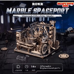 Può includere: Un kit di modelli in legno ROKR Marble Spaceport. Il kit è lungo 30.5 cm, largo 25.4 cm e alto 22.9 cm. Presenta ingranaggi, binari e un design complesso. Il kit include 472 pezzi ed è per i 14 anni e più. Il testo "Manual/Electric Mode" è visibile.