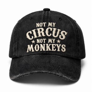 Può includere: Cappellino da baseball nero con la scritta ricamata "NOT MY CIRCUS NOT MY MONKEYS" in bianco sporco. Il cappellino ha una visiera curva e un bottone sulla parte superiore. Il tessuto è usurato.