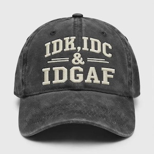 May include: A charcoal gray baseball cap with a distressed, washed-out finish. The front features embroidered off-white lettering that reads IDK, IDC & IDGAF in a bold, block-style font, centered above a horizontal line detail on the crown.