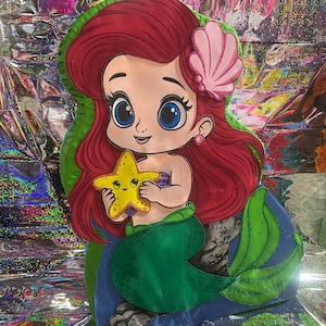 May include: A cartoon illustration of a mermaid with red hair, a pink seashell hair accessory, and a green tail. She is holding a yellow starfish. The mermaid is set against a colorful, iridescent background.