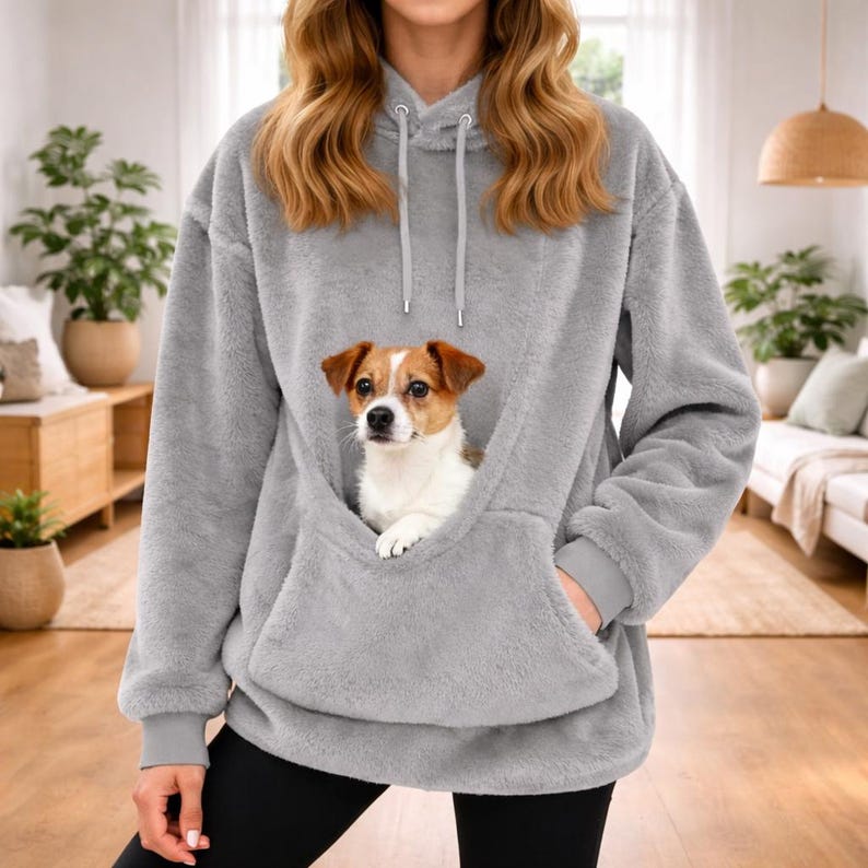 May include: A gray, oversized hoodie with a kangaroo pocket, designed to carry a small pet. The hoodie features a drawstring hood and long sleeves. A small dog with brown and white fur is nestled in the pocket.
