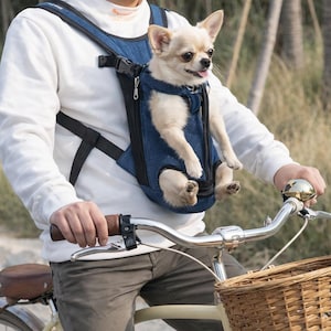 Könnte beinhalten: Ein kleiner, hellfarbiger Hund in einem blauen Denim-Rucksack für Haustiere. Die Person fährt Fahrrad. Der Rucksack hat verstellbare Träger. Das Fahrrad hat einen braunen Ledersattel und Lenker. Der Hund hat die Zunge draußen.
