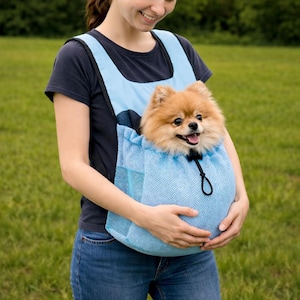 Peut inclure: Un porte-bébé bleu clair pour animaux de compagnie avec un devant en filet, conçu pour être porté comme un sac à dos. Un petit chien touffu de couleur fauve est à l'intérieur du porte-bébé. Le porte-bébé a une fermeture à cordon et des sangles noires.