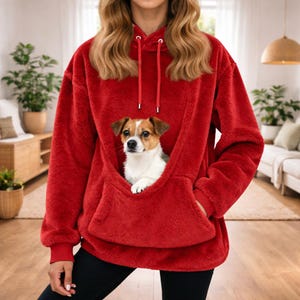 May include: A red hooded sweatshirt with a kangaroo pocket, featuring a small dog nestled inside. The dog has brown and white fur. The sweatshirt has a drawstring hood and ribbed cuffs.