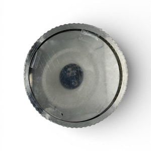 Puede incluir: Un objeto metálico circular con un borde exterior estriado y un centro oscuro. El objeto parece estar hecho de un material metálico cepillado, con una superficie ligeramente reflectante. El diseño es simple y funcional.