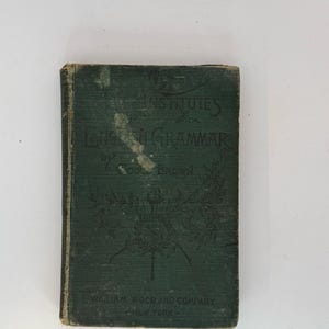 Könnte beinhalten: Ein altes, dunkelgrünes Buch mit dem Titel "Institutes of English Grammar" von Goold Brown. Das Buchcover zeigt verzierte florale Designs und den Namen des Verlags, William Wood and Company, New York.