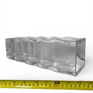 May include: A clear, rectangular glass vase with a wavy top edge. The vase is approximately 14 inches long. The image is taken against a white background, with a yellow measuring tape in the foreground.
