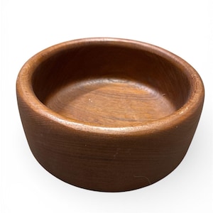 Könnte beinhalten: Eine kleine, runde Holzschale in einem satten, dunkelbraunen Farbton. Die Schale hat eine glatte, polierte Innenseite und eine leicht strukturierte Außenseite. Die Holzmaserung ist sichtbar und unterstreicht die natürliche Ästhetik. Geeignet für Snacks oder kleine Portionen.