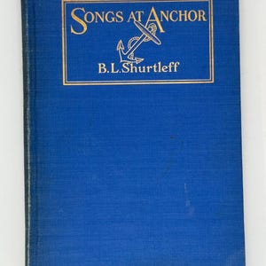 Puede incluir: Un libro antiguo titulado "Songs at Anchor" de B.L. Shurtleff. La portada es de color azul oscuro con letras doradas y una ilustración de ancla. La cubierta del libro tiene una apariencia texturizada.
