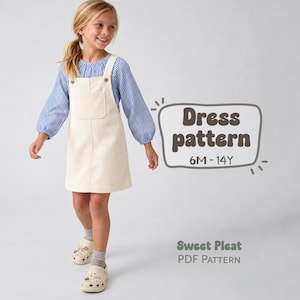 May include: A cream-colored pinafore dress with a front pocket and button straps, worn over a blue and white striped long-sleeve shirt. The text reads Dress pattern 6M-14Y and Sweet Pleat PDF Pattern in a dark brown font on a light background.