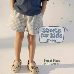 Könnte beinhalten: Ein Kind trägt Shorts mit Hahnentrittmuster und beige Clogs mit Obst- und Gemüseanhängern. Die Shorts sind hellgrau und weiß. Das Bild enthält den Text "Shorts for kids 2T-14Y" und "Sweet Pleat PDF Pattern".