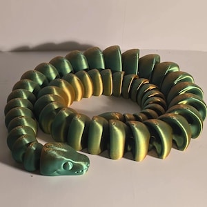 May include: A 3D-printed articulated snake toy in shades of green and gold. The snake's head features eye details, and the body is segmented, allowing for flexible movement. The toy is designed to be a fun and interactive item.