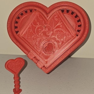 May include: A red heart-shaped box with a matching key. The box has a detailed design on the front and a small heart-shaped keyhole. The key is also heart-shaped with a decorative handle. The box is open, revealing the interior.