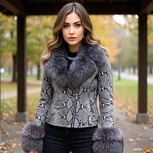 Könnte beinhalten: Graue Jacke mit Schlangenmuster und Pelzkragen und -bündchen. Die Jacke hat einen Reißverschluss und ein schwarzes Futter. Das Model trägt ein schwarzes Oberteil und eine schwarze Hose. Der Hintergrund ist ein Park mit Bäumen.