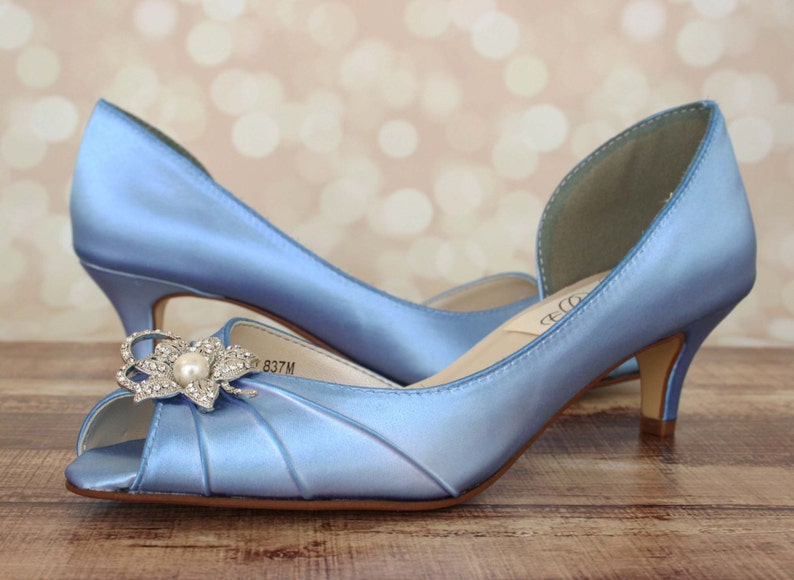May include: A pair of light blue satin peep-toe heels with a rhinestone flower embellishment. The heels are approximately 2.5 inches tall.