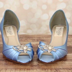 May include: A pair of light blue satin peep-toe heels with a rhinestone and pearl embellishment. The heels are labeled "Ellie Shoes".