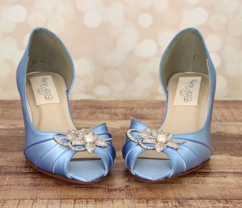 May include: A pair of light blue satin peep-toe heels with a rhinestone and pearl embellishment. The heels are labeled "Ellie Shoes".