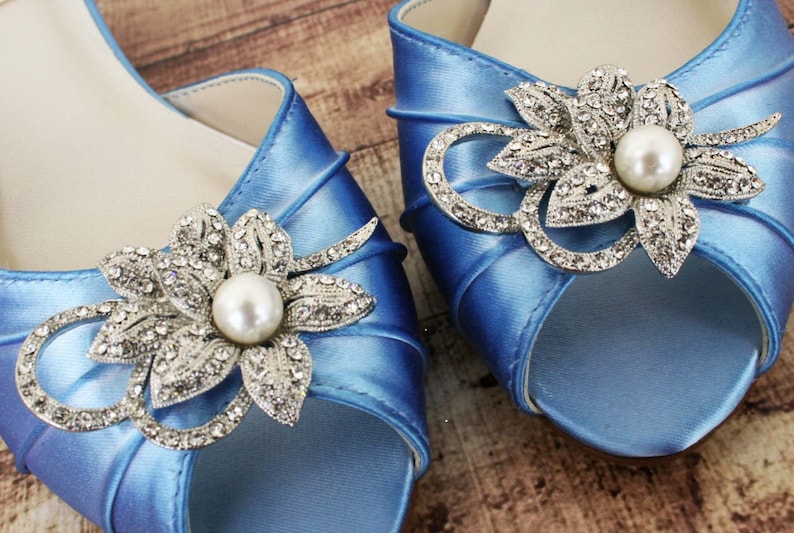 May include: A pair of light blue satin bridal shoes with a jeweled flower embellishment on each toe. The flowers are silver with a pearl center.