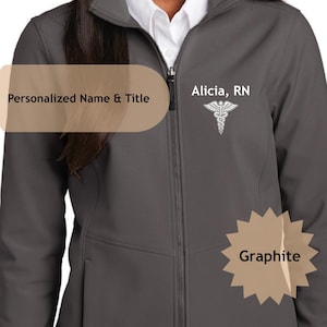 May include: Graphite-coloured zip-up jacket with the text "Alicia, RN" and a medical symbol. The jacket features a personalized name and title area. The jacket is a softshell style.