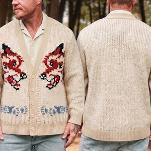 Puede incluir: Cárdigan beige con cuello en V y cierre de botones. El frente del cárdigan presenta un diseño rojo y negro, con patrones azules y blancos en la parte inferior. La parte trasera es de color beige liso.