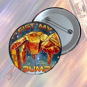 May include: A round button with a colorful design featuring a stylized crab-like figure in shades of red, orange, and yellow against a starry blue background. The text "FIST MY BUMP" and "PROJECT HAIL MARY" are also visible.