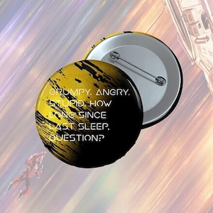 Può includere: Un bottone rotondo con un design nero e giallo e il testo "GRUMPY. ANGRY. STUPID. HOW LONG SINCE LAST SLEEP, QUESTION?" Il bottone ha una spilla metallica sul retro.