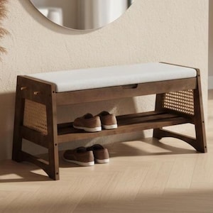 May include: A wooden shoe bench with a white cushioned seat and a lower shelf. The bench has a dark brown finish and woven cane detailing on the sides. Two pairs of brown shoes are placed on the shelf.