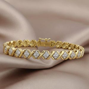 Può includere: Un braccialetto dorato con un motivo a X e diamanti ripetuto. Ogni sezione a forma di diamante è riempita di piccole pietre scintillanti. Il braccialetto è esposto su una superficie satinata beige.