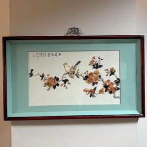 May include: A rectangular wall art piece featuring a three-dimensional relief of a bird perched on a flowering branch. The artwork is set against a white background with a light blue mat, enclosed in a dark wood frame with black Chinese calligraphy.