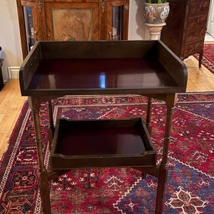 May include: A dark brown wooden side table featuring a rectangular top with a raised back and side gallery edges. The table includes a lower shelf with a shallow tray design, supported by four slender, straight legs with a smooth, polished finish.